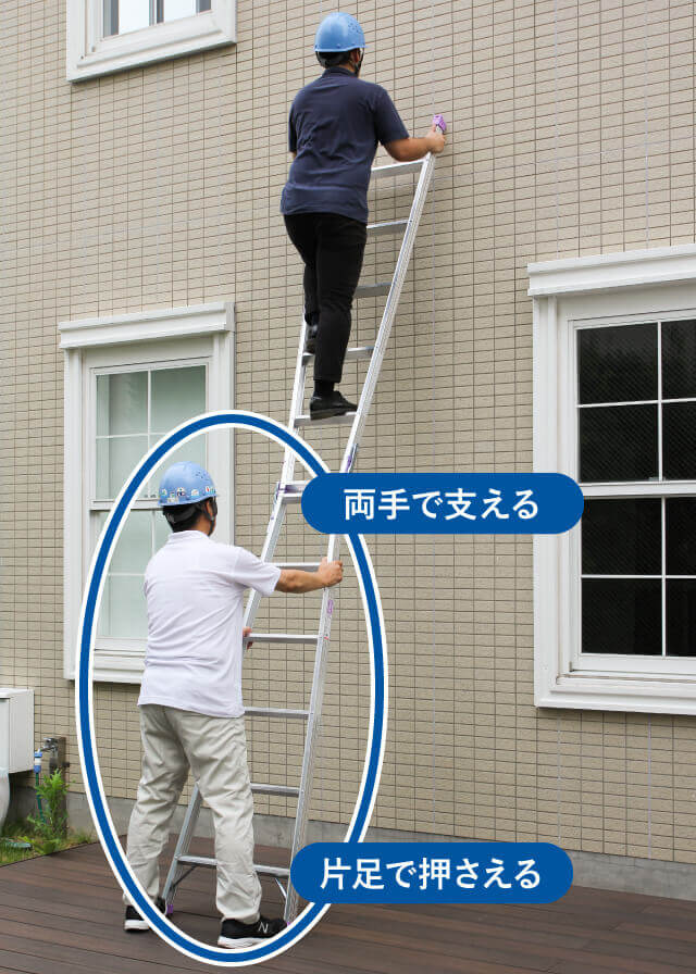 補助者ははしごの脚を片足で押さえ、両手でしっかりとはしごを支えます。